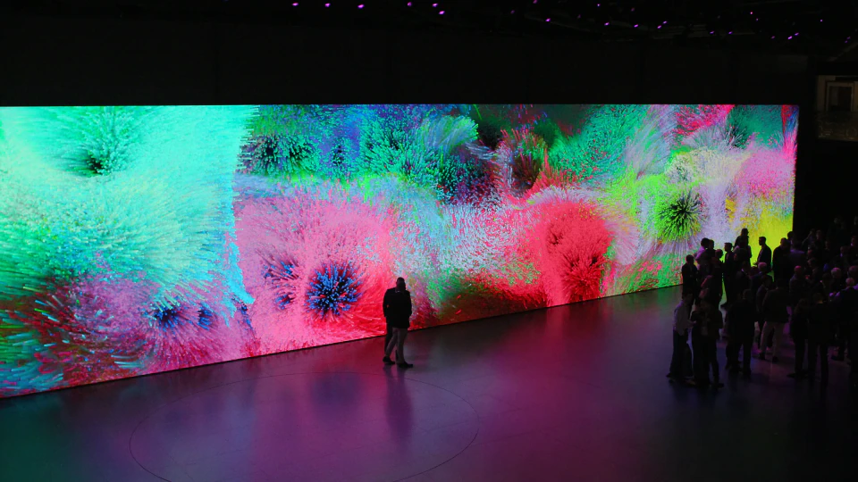 Wide view of the Volkswagen Group booth at IAA Mobility 2025 — realtime generative particle visuals filling the 14,000 × 2,000 px LED wall as visitors gather in front